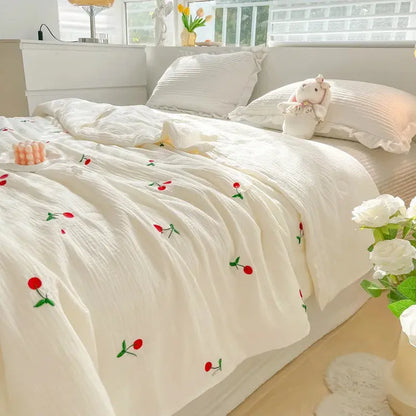White floral embroidered comforter on a bed with pillows and flowers.