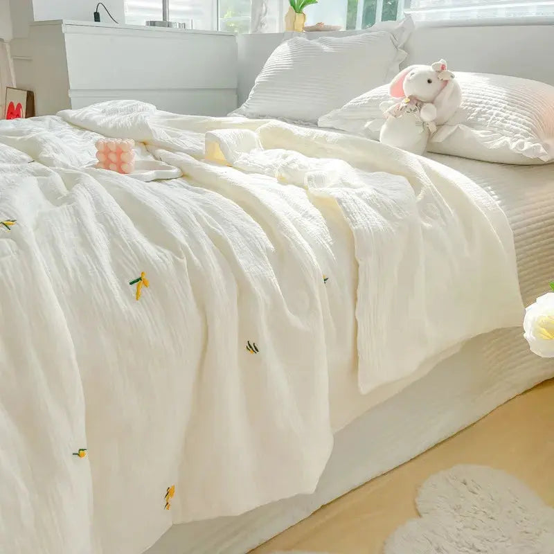 White textured comforter on a bed with decorative pillows and a teddy bear in a bright bedroom.