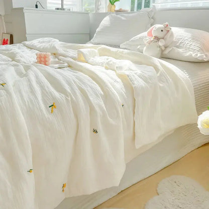 White textured comforter on a bed with decorative pillows and a teddy bear in a bright bedroom.