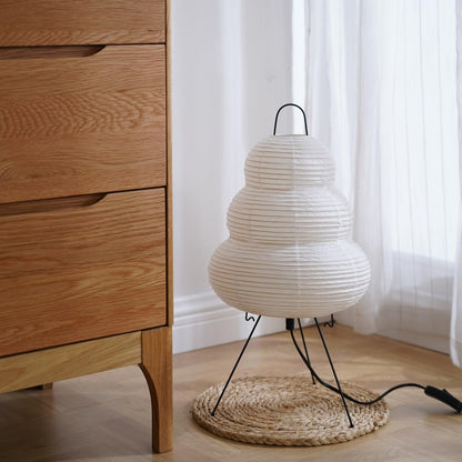 White textured lamp on a woven mat next to a wooden dresser with sheer curtains in the background.
