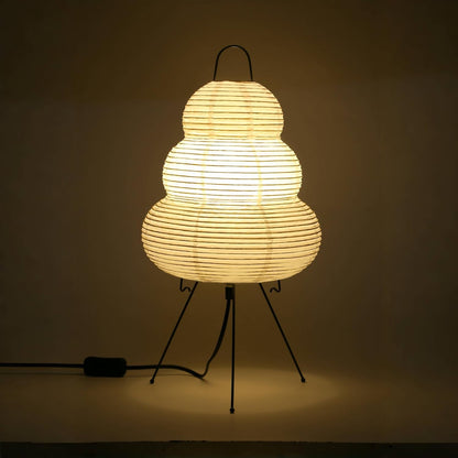 Woven lamp on a stand with a warm glow against a dark background