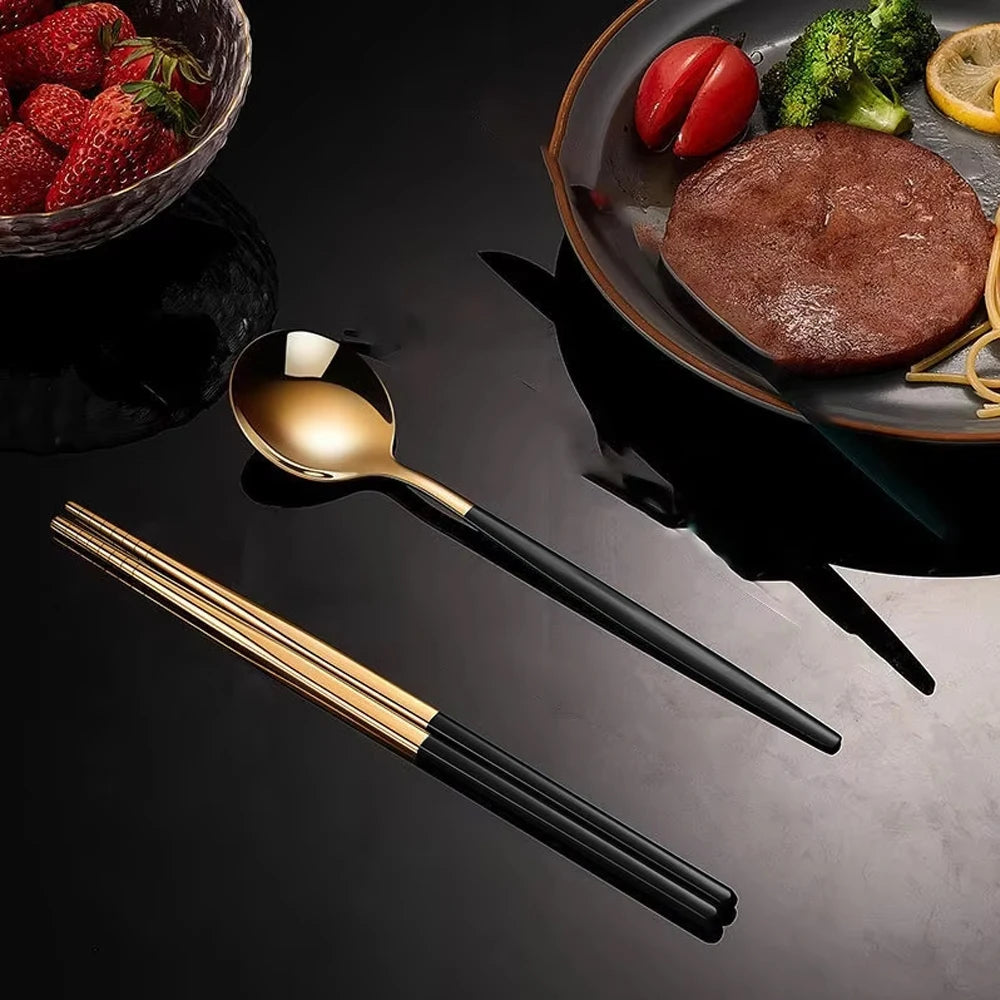 Black and gold cutlery set on a dark surface with food in the background
