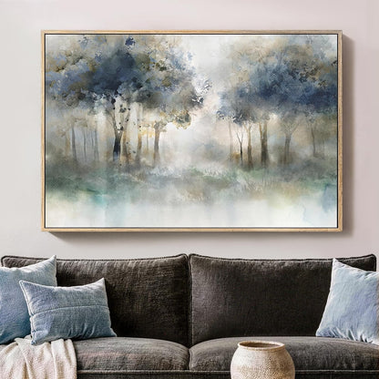 A framed watercolor painting of a misty forest with blue, gray, and white tones, displayed on a light beige wall above a dark gray sofa with blue pillows.