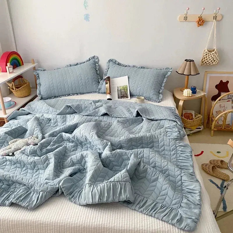 Light blue quilt and pillow set on a bed in a bedroom with decor elements.