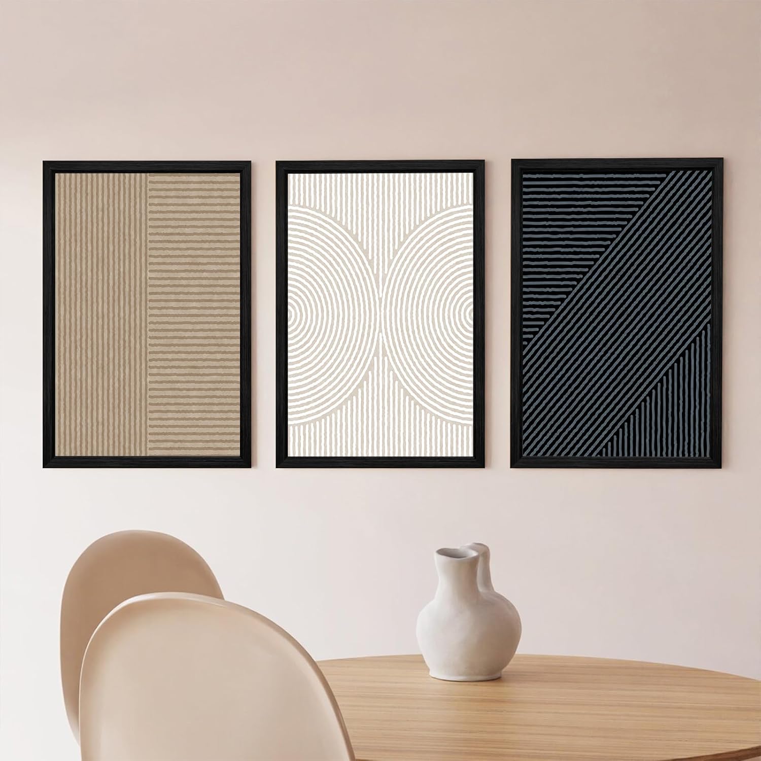 Three abstract art prints on a wall above a table with a vase.