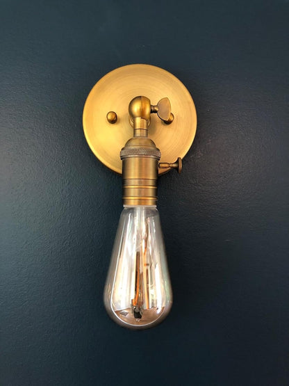 Brass wall sconce with a clear light bulb on a dark blue wall