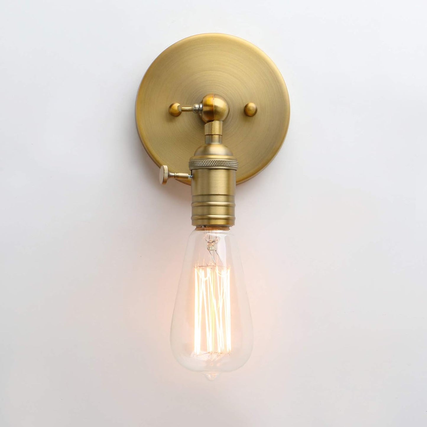 Brass wall sconce with a lit filament bulb on a white background