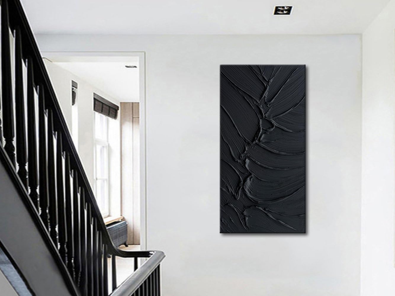 Black abstract wall art on a white wall next to a staircase