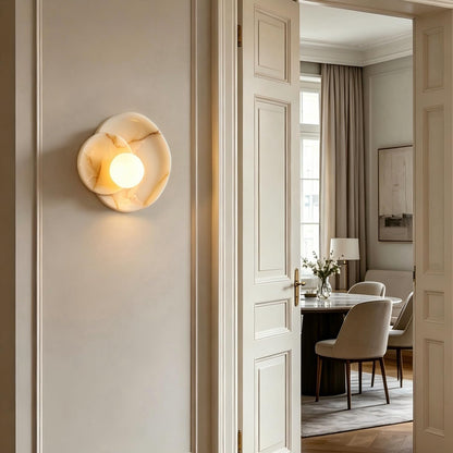 Decorative wall light fixture on a neutral wall with a softly lit room in the background.