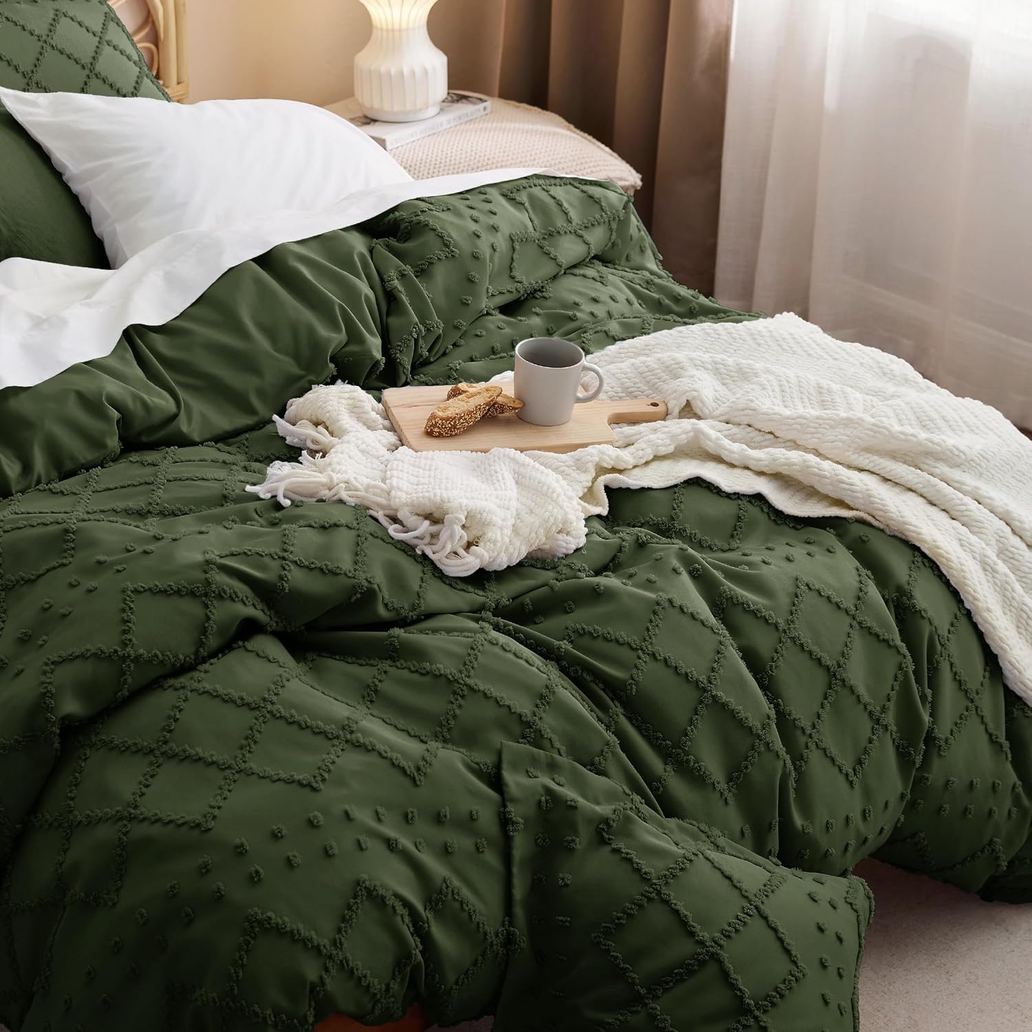 Green textured comforter on a bed with a cup of coffee and cookies.