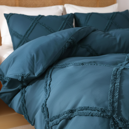 A close-up of a teal blue quilted bedding set with textured fringe details, styled on a bed with a tan headboard and white pillows.