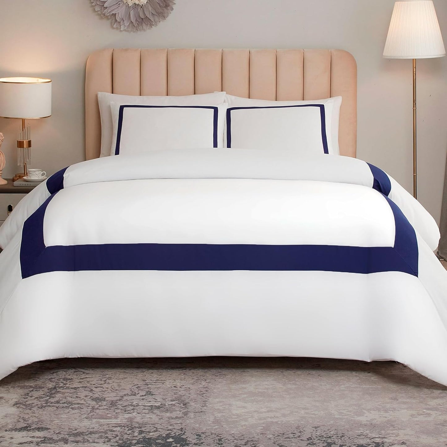 A neatly made bed with a white comforter set featuring bold navy blue horizontal stripes and matching pillow shams, styled in a bedroom with a beige tufted headboard, bedside lamps, and a gray rug.