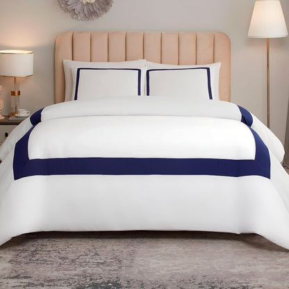 A neatly made bed with a white comforter set featuring bold navy blue horizontal stripes and matching pillow shams, styled in a bedroom with a beige tufted headboard, bedside lamps, and a gray rug.