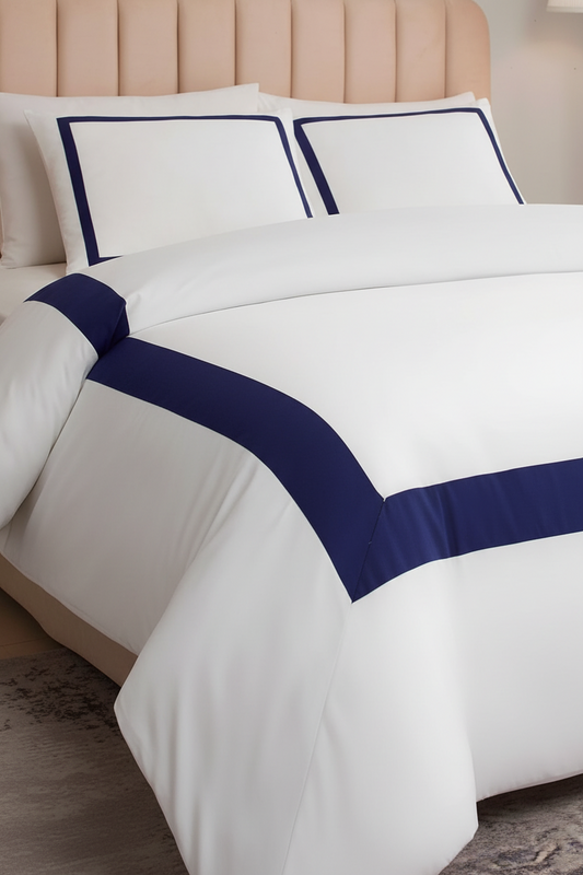 White bedding set with navy blue border trim on a bed, featuring two matching pillowcases and a duvet cover, styled with a beige tufted headboard.