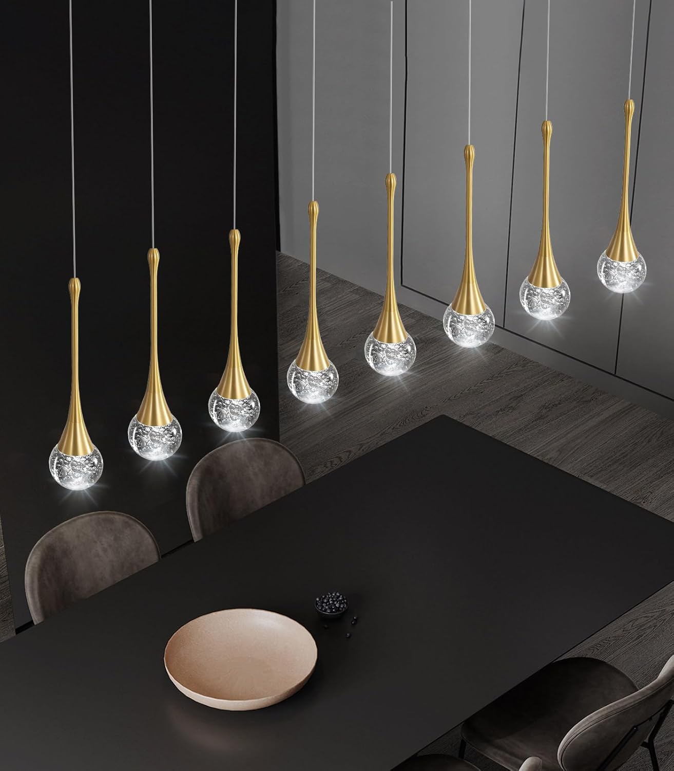 Modern pendant lights hanging above a dining table in a darkly decorated room.
