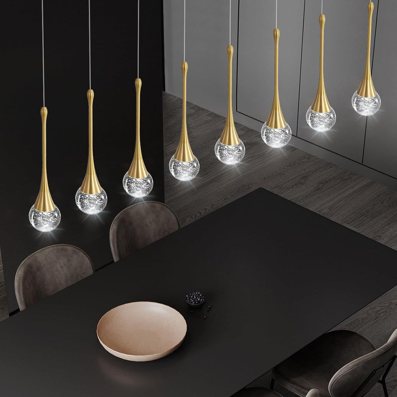 Modern pendant lights hanging above a dining table in a darkly decorated room.
