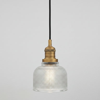 A vintage-style industrial pendant light with a clear ribbed glass dome shade, a brass metal socket, and a black hanging cord, shown against a plain white background.