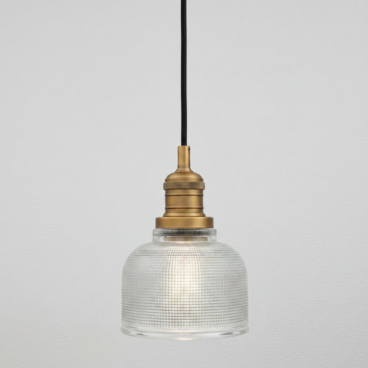 A vintage-style industrial pendant light with a clear ribbed glass dome shade, a brass metal socket, and a black hanging cord, shown against a plain white background.