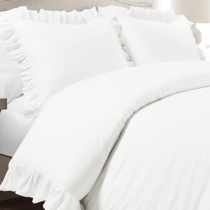 White ruffled bedding set on a bed, including a duvet cover and matching pillow shams, styled in a softly lit bedroom setting.