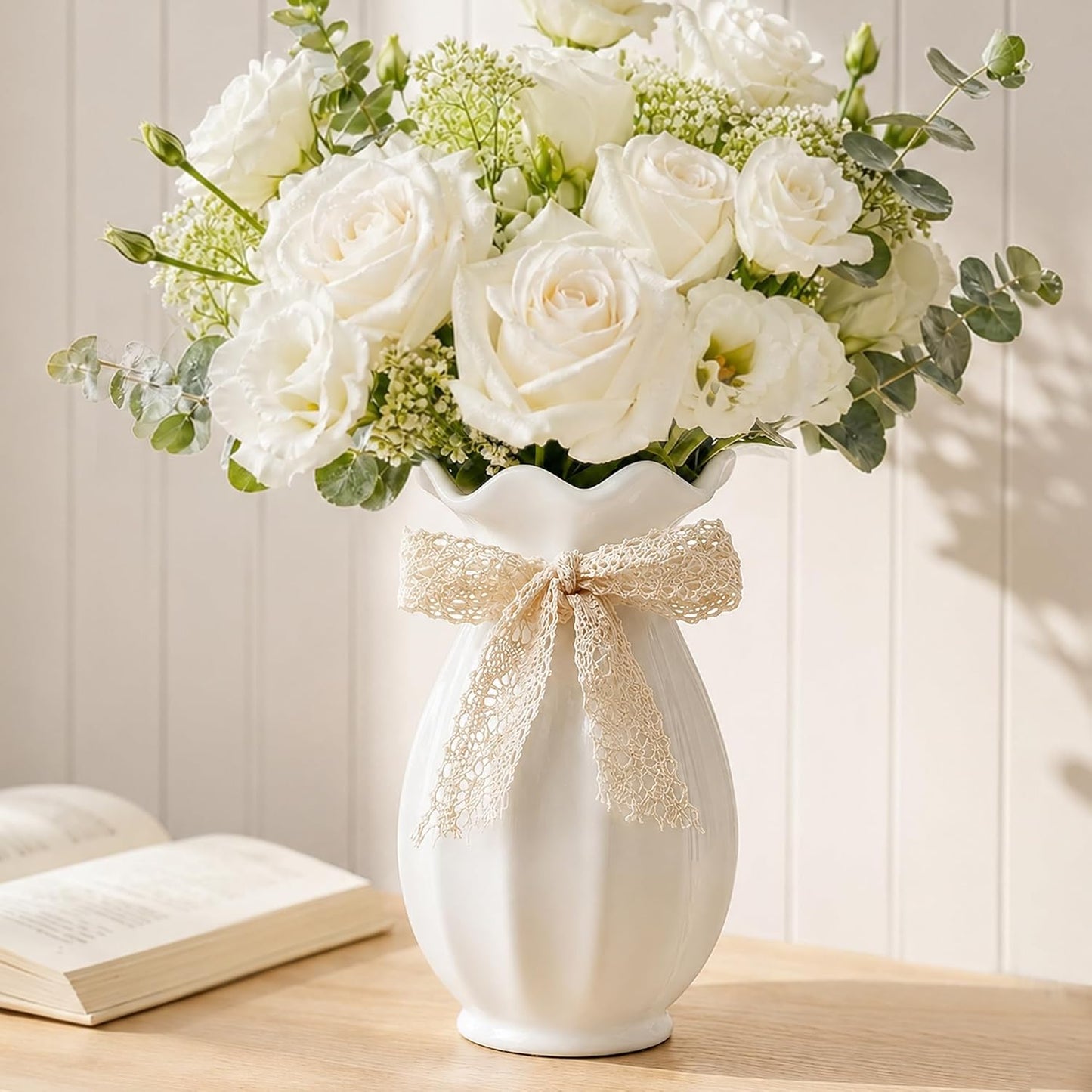 White vase with a decorative bow and bouquet of white flowers on a wooden surface.