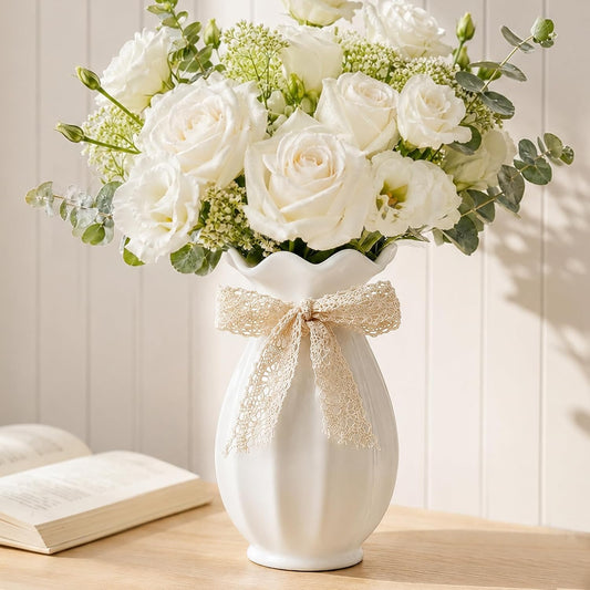 White vase with a decorative bow and bouquet of white flowers on a wooden surface.