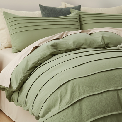 A sage green pleated bedding set, including a duvet cover and matching pillowcases, styled on a bed with cream pillows and a dark gray accent pillow.