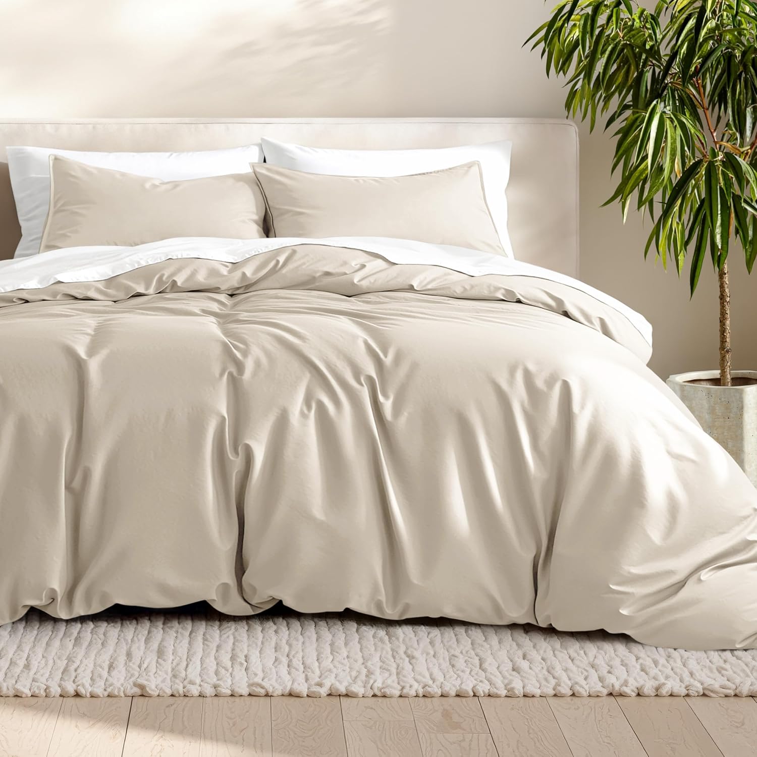 Beige bedding set on a bed with white pillows and a plant in the corner.