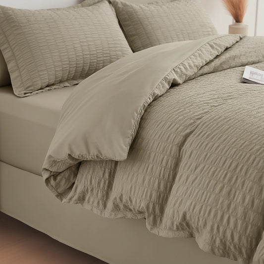 A beige textured bedding set on a bed, featuring a crinkled quilt and matching pillowcases in a neutral warm beige tone.