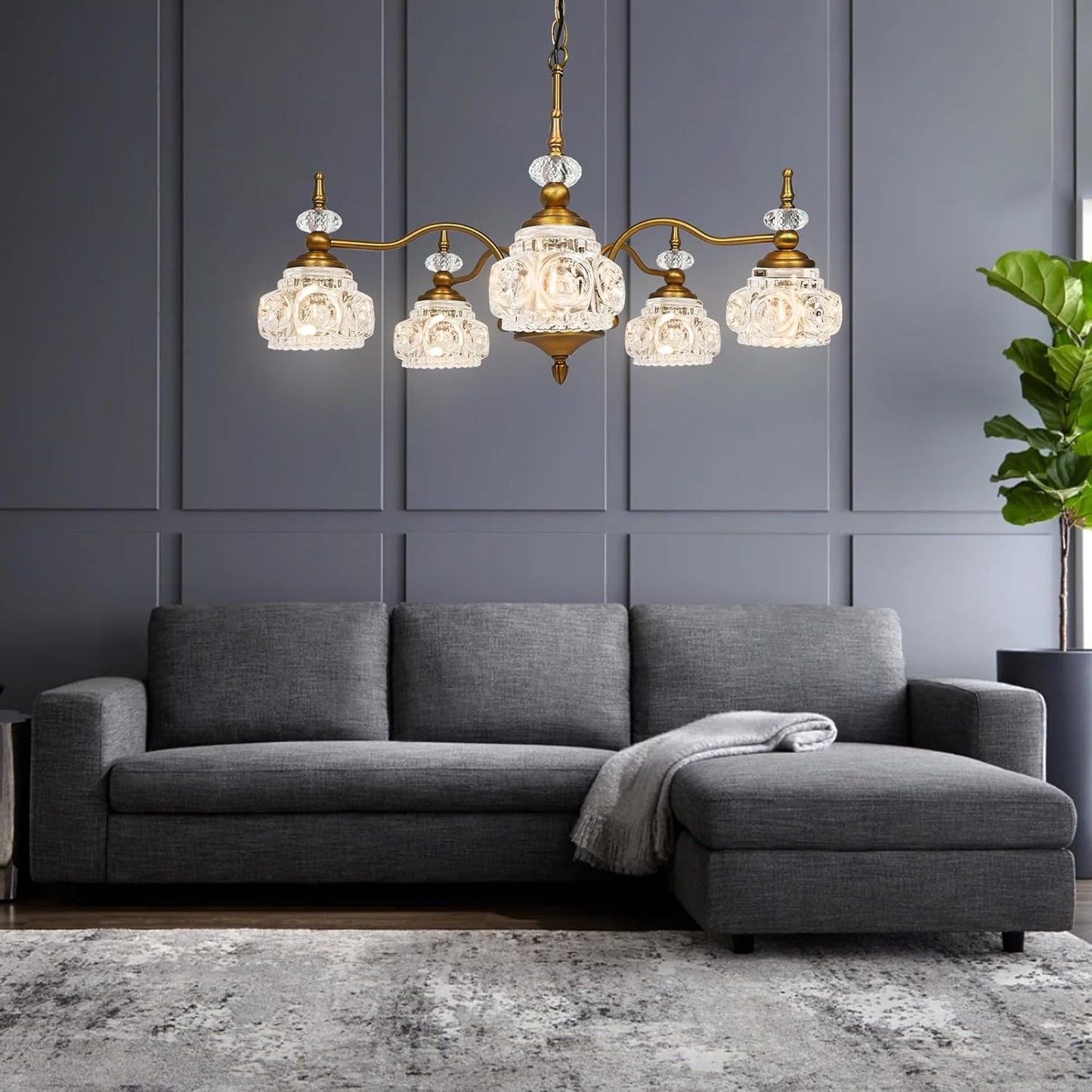 Gray sectional sofa with a decorative chandelier in a room with gray walls and a plant.