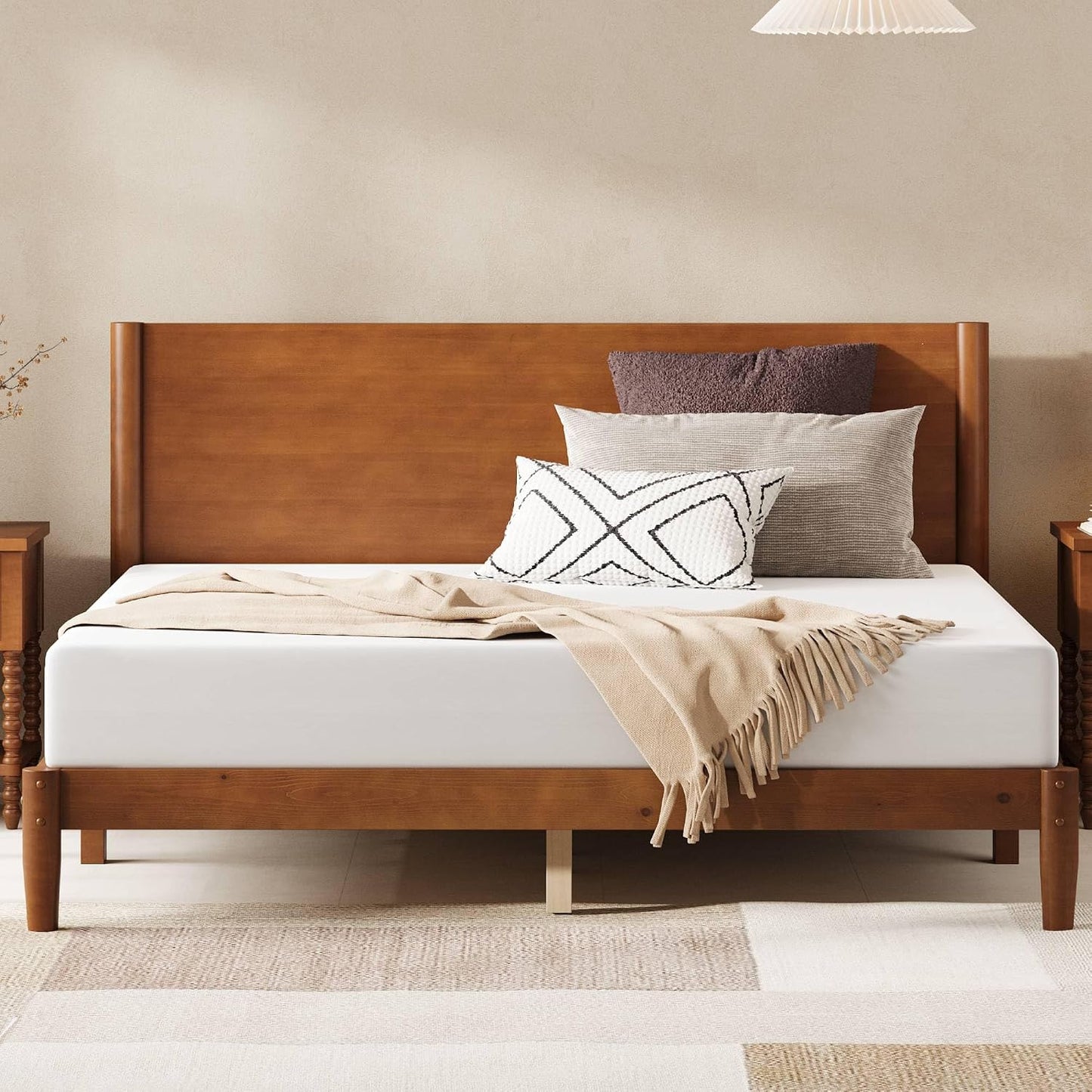 Wooden bed with white mattress, beige blanket, and patterned pillows in a room.