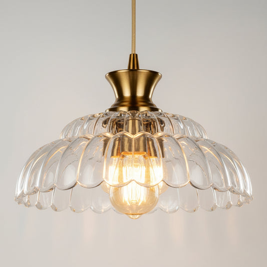 A vintage-style pendant light with a clear glass scalloped dome shade and a polished brass-toned metal top and cord, glowing with a warm light against a solid black background.