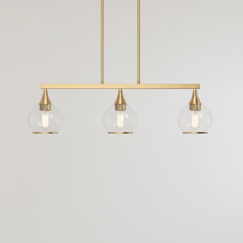 A modern three-light linear pendant chandelier with a brushed brass/gold horizontal bar, three clear glass globe shades, and visible Edison-style bulbs, shown against a textured beige wall.