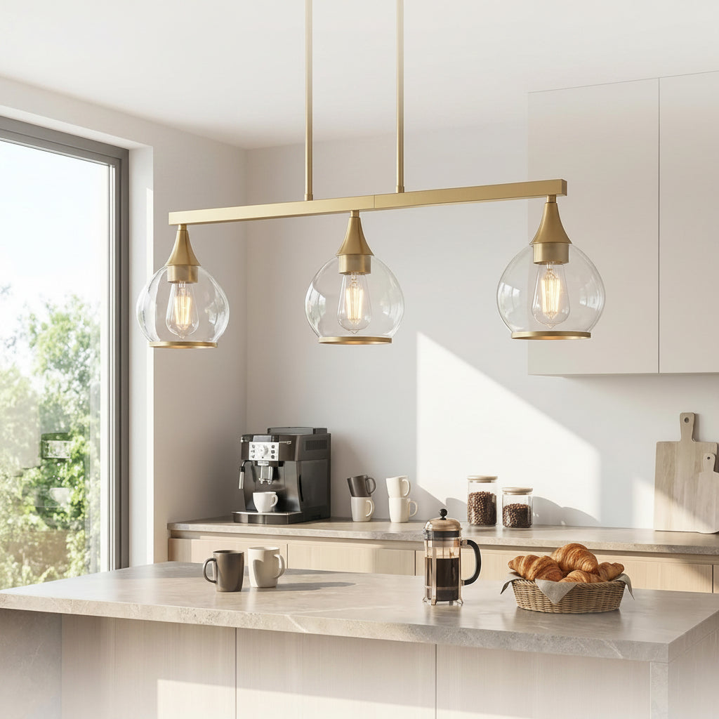 A modern three-light linear pendant lamp with clear glass globe shades and brushed brass hardware hangs over a kitchen counter. The scene includes text reading 'MORNING RITUAL' and 'Bright light for your home coffee station,' plus icons and text about coffee station use, warm glow, and adjustable height.