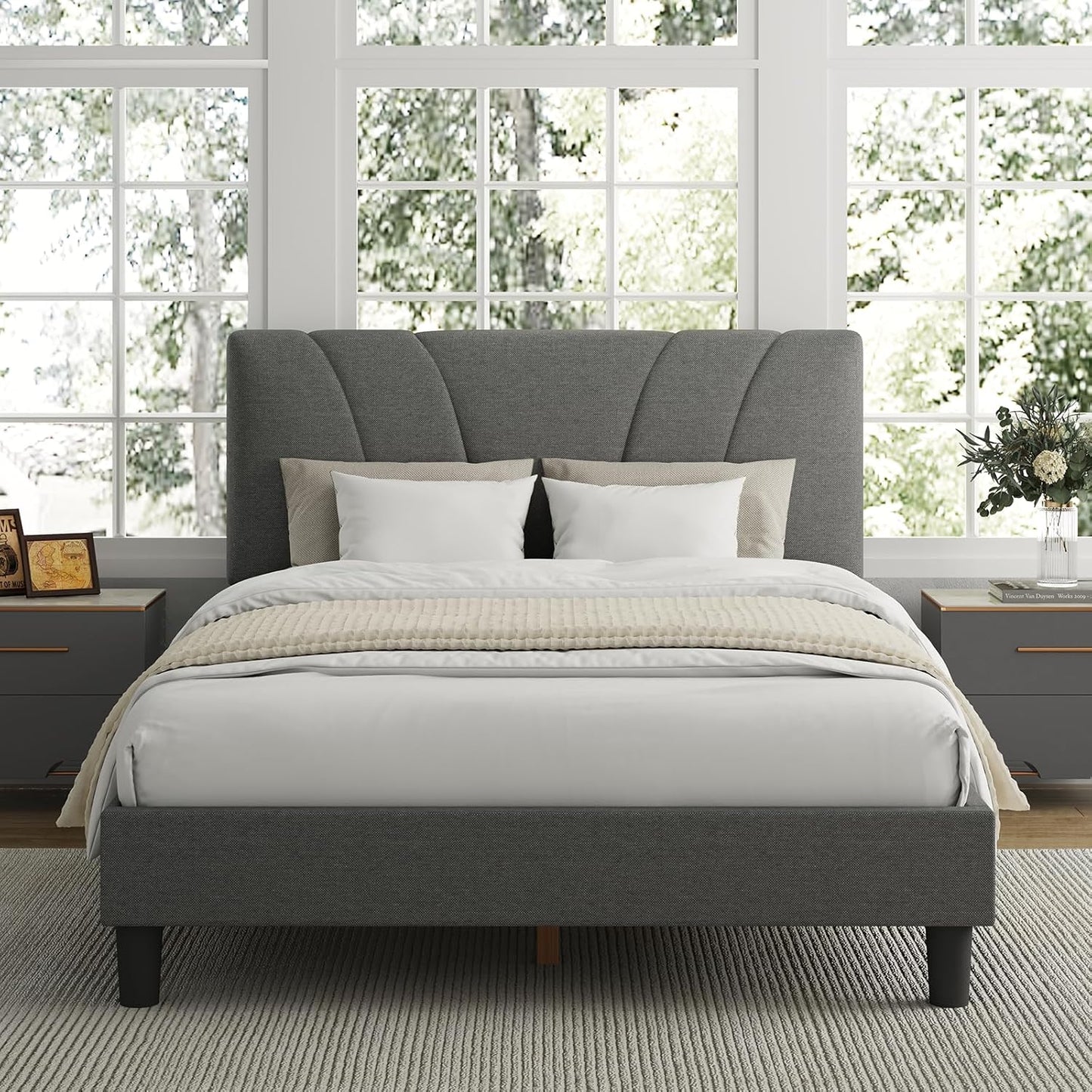 Gray upholstered bed in a bright bedroom with large windows.