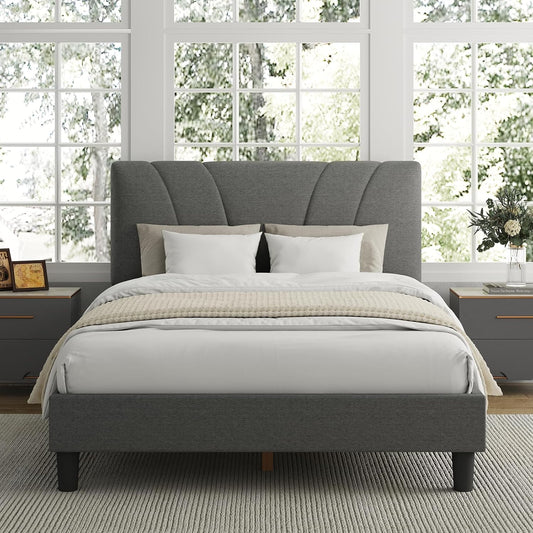 Gray upholstered bed in a bright bedroom with large windows.
