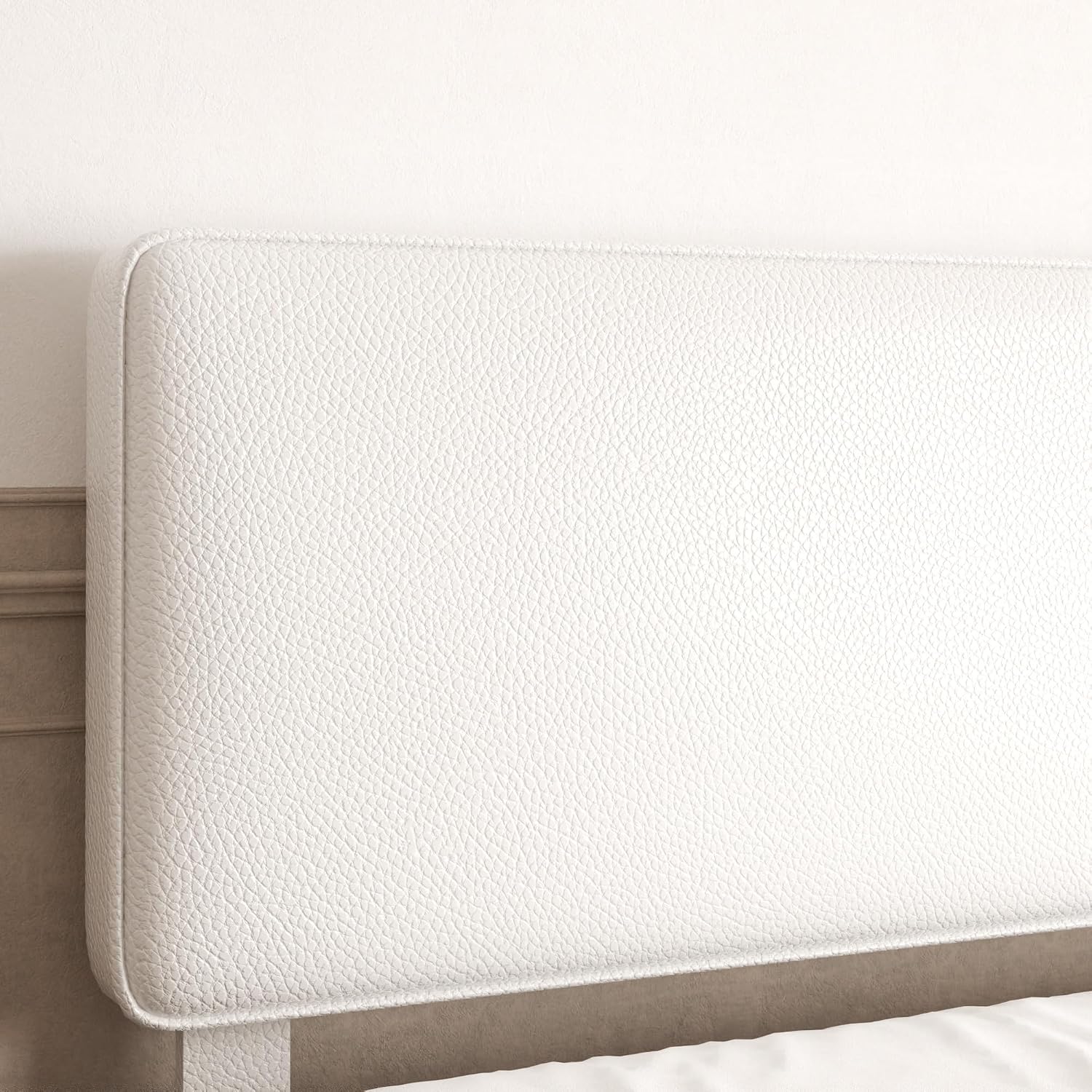 Close-up of a white upholstered headboard with a textured pebbled leather or faux-leather finish, shown against a light neutral wall.