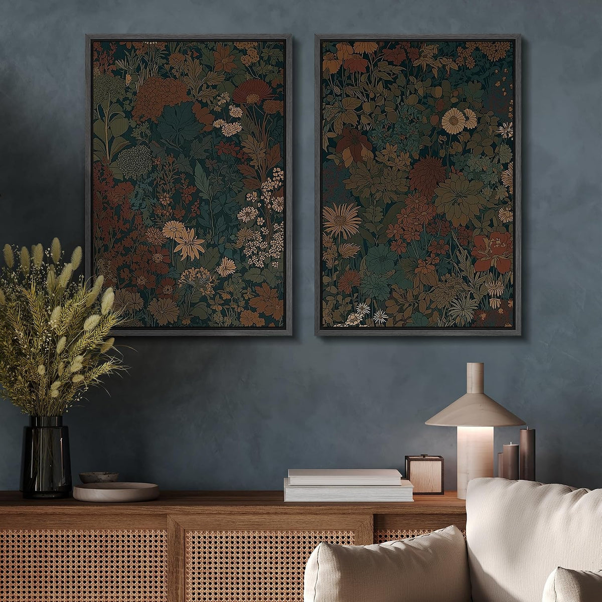 Two vertical framed botanical art prints with dense floral patterns in muted earthy tones, displayed side by side on a textured blue-gray wall above a wooden console table with a lamp and books.