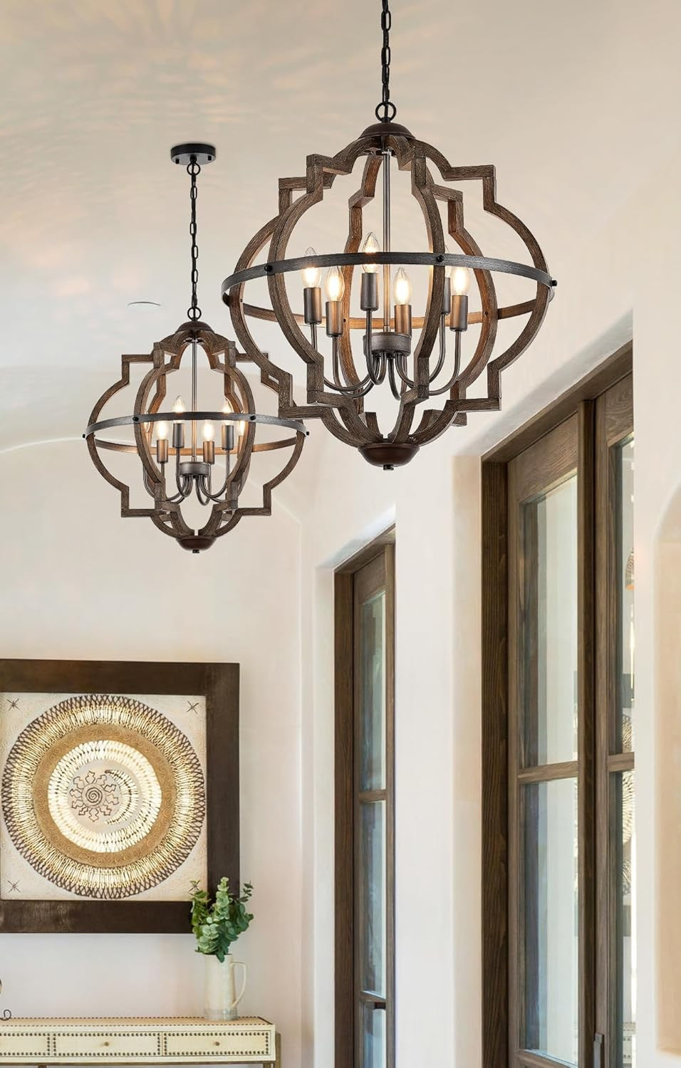 Two ornate chandeliers hanging in a room with a decorative wall piece and plant.