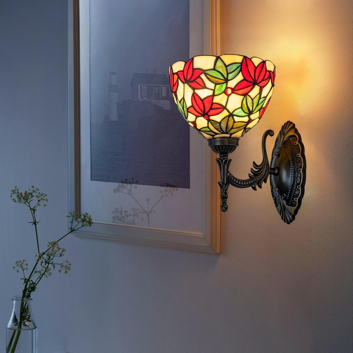 Decorative wall lamp with stained glass design on a wall next to a framed picture.