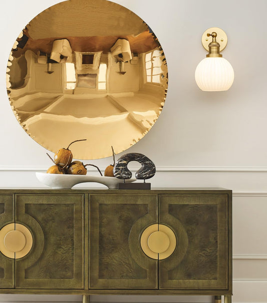 Round gold mirror above a wooden cabinet with decorative items.