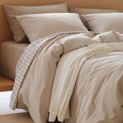 A neatly made bed with beige and cream bedding, including a striped duvet cover, matching pillowcases, and a folded cream sheet, set against a warm wood headboard and beige wall.