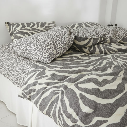 A bedding set with a zebra print duvet cover and matching pillowcases alongside a leopard print pillowcase, styled on a bed in a bright, minimalist bedroom.