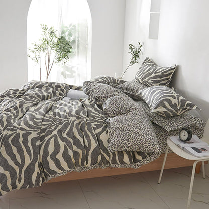 A bed dressed in a zebra-print and leopard-print bedding set, styled in a bright, modern bedroom with white walls, a small side table, and potted plants.