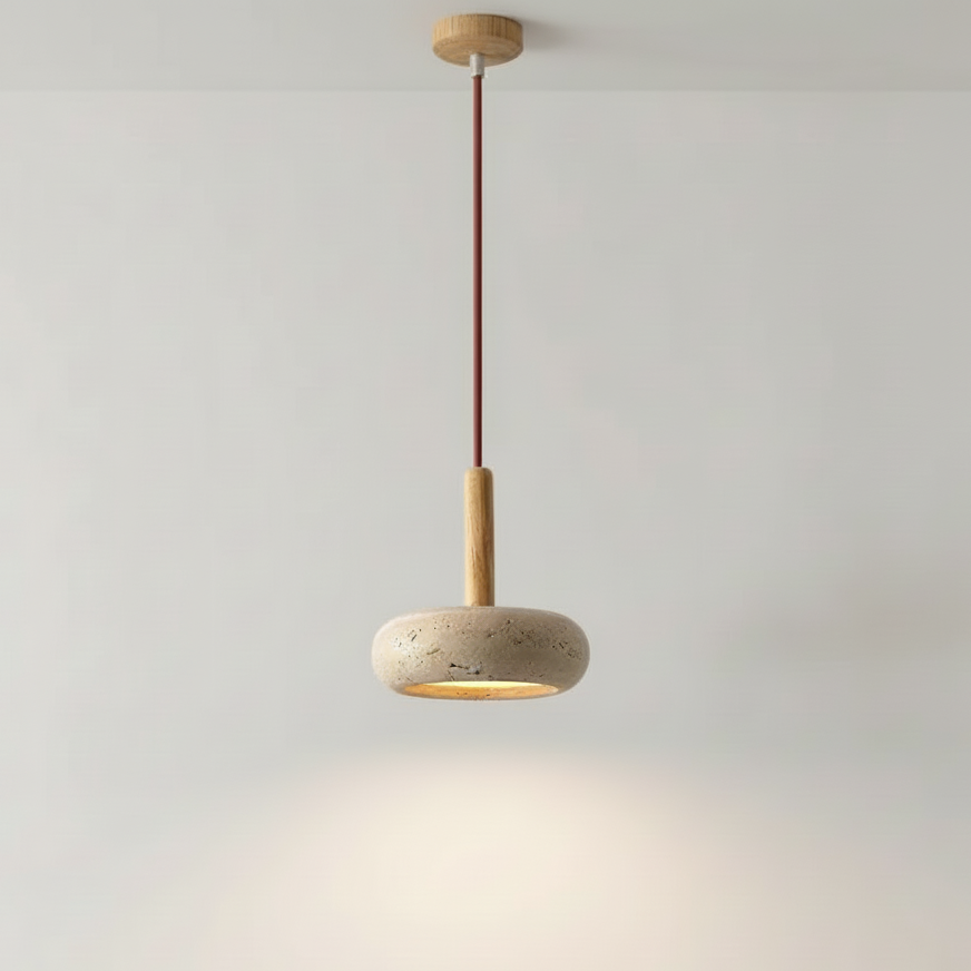 A modern pendant light with a round textured stone shade, a light wood stem, and a dark brown cord, suspended against a plain light gray wall.