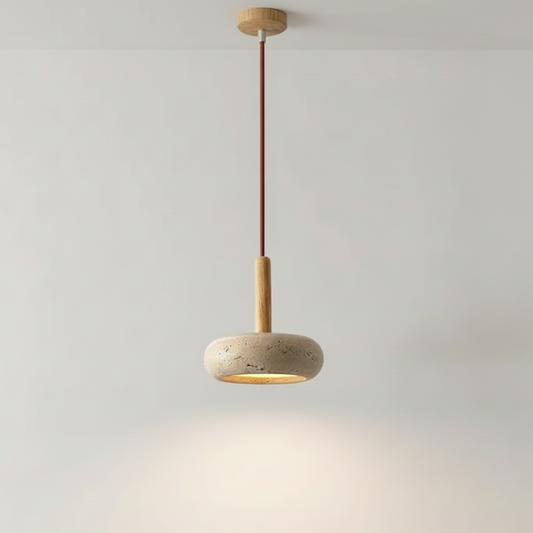 A modern pendant light with a round textured stone shade, a light wood stem, and a dark brown cord, suspended against a plain light gray wall.