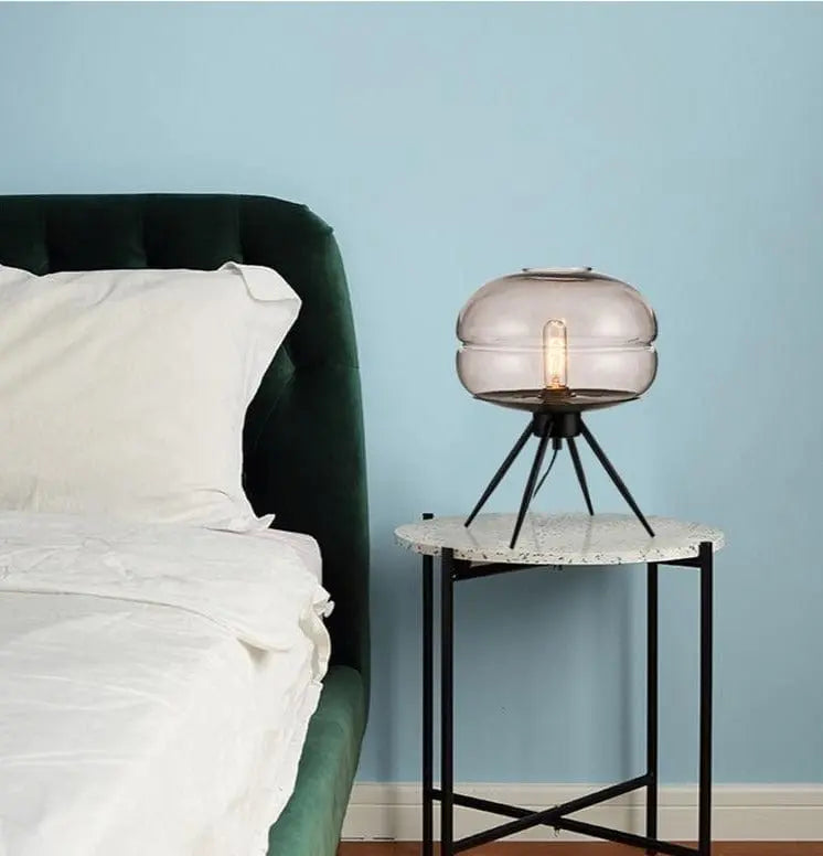 Bedroom with a bed and a side table with a lamp against a light blue wall.